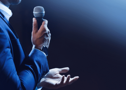 Medical staffing professional delivering a confident speech on stage with a microphone.