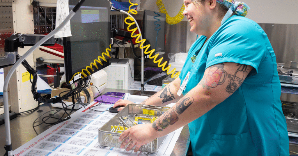 This image features a sterile processing technician performing a detailed inspection of surgical instruments in a hospital decontamination area. Proper handling, assembly, and evaluation of medical devices are core competencies covered by sterile processing certifications, which validate a technician’s ability to ensure infection prevention and regulatory compliance. Ongoing training and visual assessments like this are essential for passing certifications and maintaining quality standards in healthcare facilities.