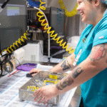 This image features a sterile processing technician performing a detailed inspection of surgical instruments in a hospital decontamination area. Proper handling, assembly, and evaluation of medical devices are core competencies covered by sterile processing certifications, which validate a technician’s ability to ensure infection prevention and regulatory compliance. Ongoing training and visual assessments like this are essential for passing certifications and maintaining quality standards in healthcare facilities.