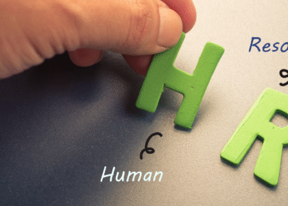 Close-up of a hand placing green letters “H” and “R” to form “HR” representing Human Resources in a healthcare organization.