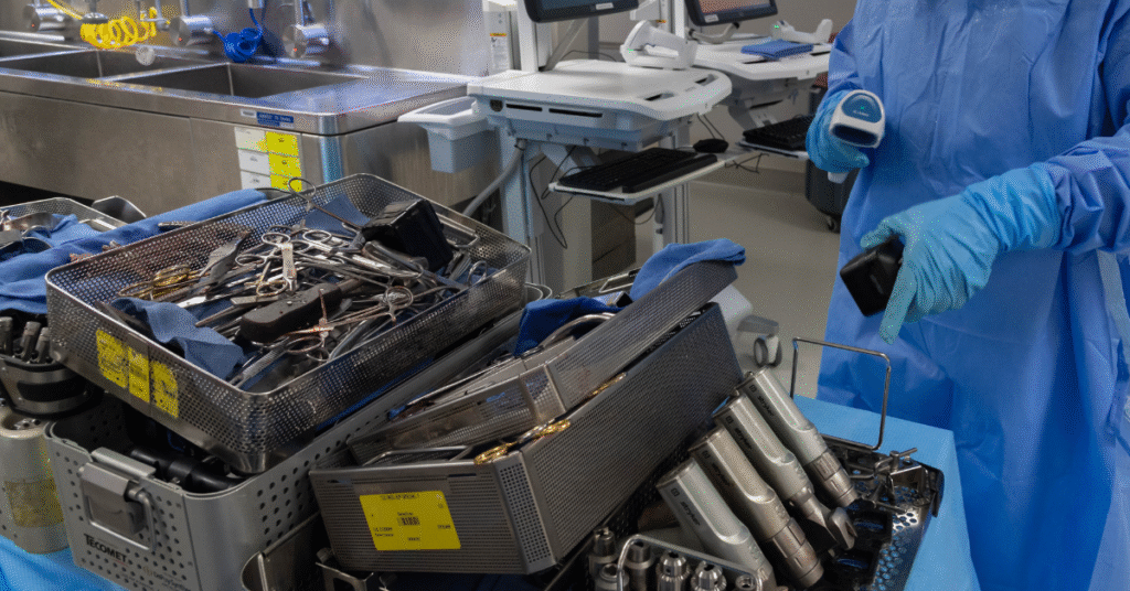 Sterile processing technician scanning surgical instruments in a decontamination area, following AAMI reprocessing standards.