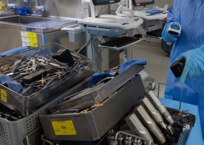 Sterile processing technician scanning surgical instruments in a decontamination area, following AAMI reprocessing standards.