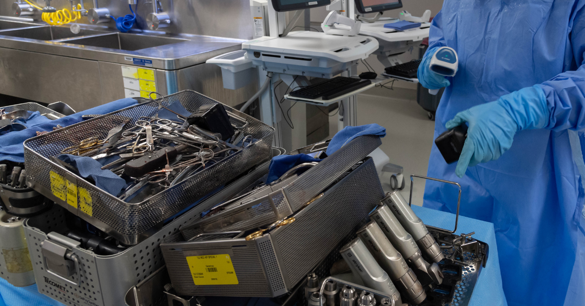 Sterile processing technician scanning surgical instruments in a decontamination area, following AAMI reprocessing standards.