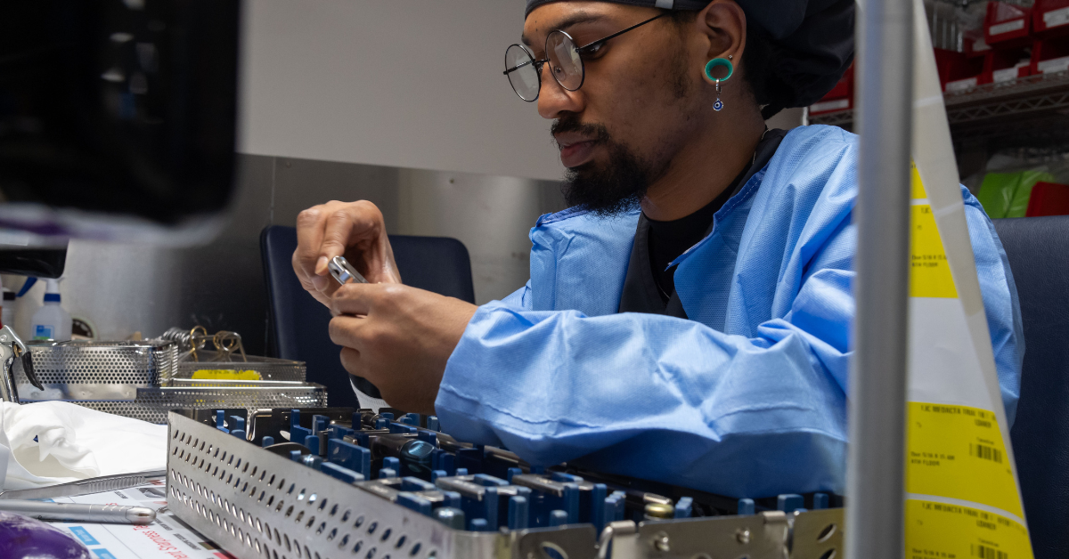 Sterile processing technician inspecting surgical instruments in a sterile environment.