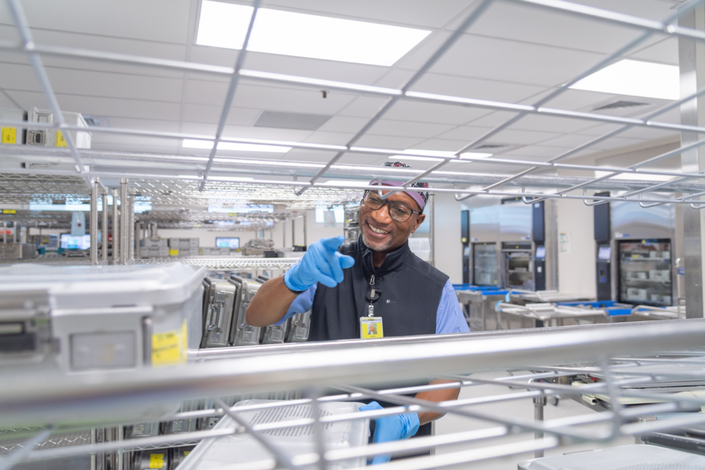 Sterile processing technician handling surgical instrument trays in a hospital SPD department during sterile processing and workflow operations.